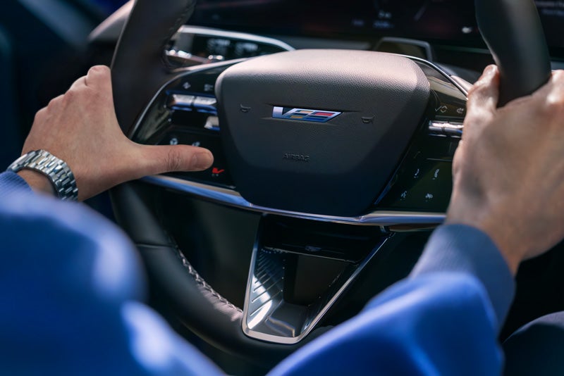 Close-up of a Man About to Press the V-Button on the 2026 OPTIQ-V Steering Wheel | Cadillac of Santa Fe in Santa Fe NM